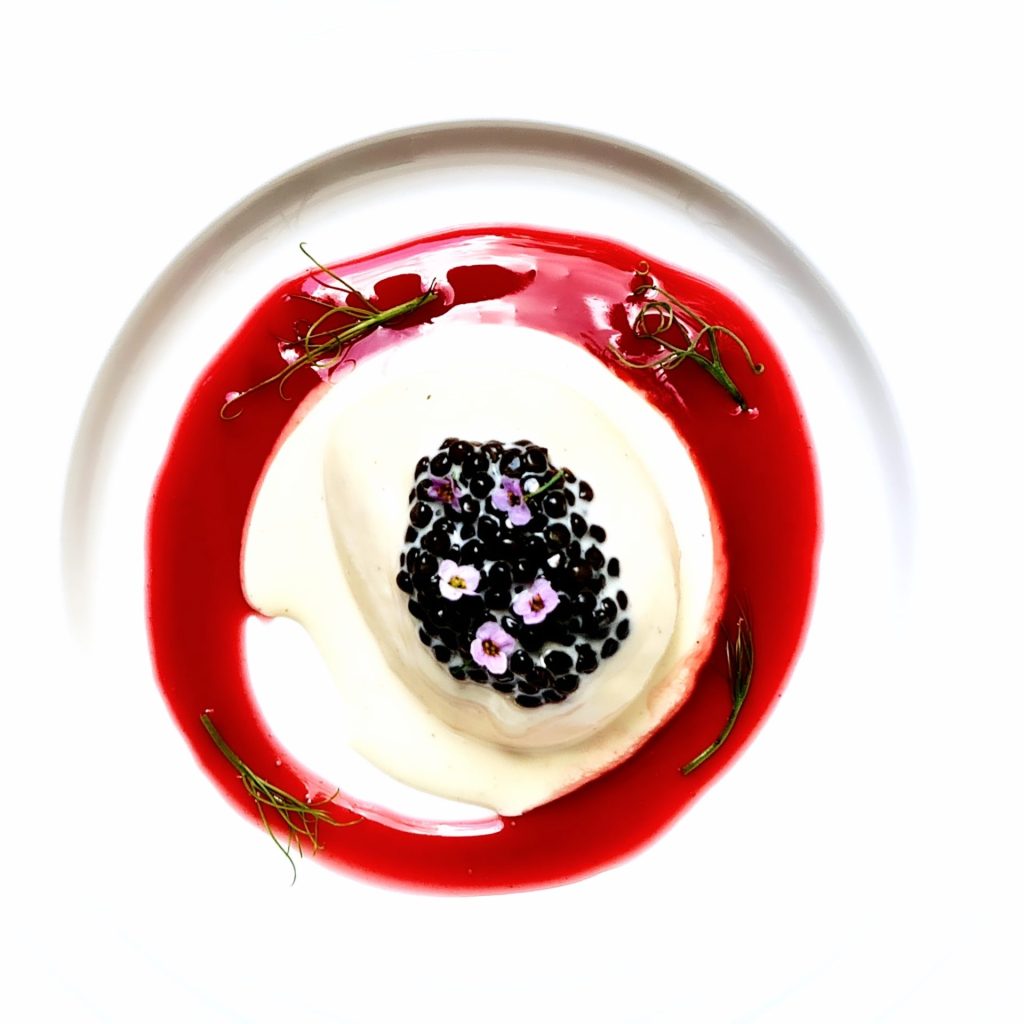 Ein weißer Teller mit einem Dessert, garniert mit frischen Brombeeren.